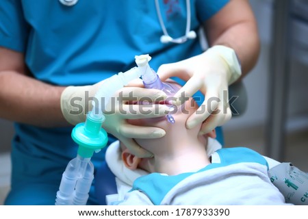 The anaesthetist holds a breathing mask on the child's face.Preparation for dental surgery. General anesthesia. Treatment of multiple caries of baby teeth. The device of artificial ventilation of lung