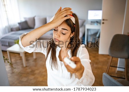 Woman feeling bad for summer heat haze.Millennial woman at home exhausted by hot weather closed eyes feels unwell dying of heat holding in hand remote control using it for reducing too hot temperature Royalty-Free Stock Photo #1787934023