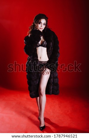 Beautiful woman wearing luxury dark faux mink fur coat. Winter fashion model posing. editorial image for advertisment in a magazine. Full length portrait of a model on red background in studio
