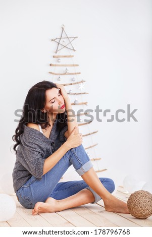 Beautiful brunette girl sitting near original Christmas tree of twigs and sticks