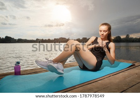 A young athletic teen girl is doing fitness aerobics against the background of a lake on a clear Sunny day. The concept of a healthy lifestyle.