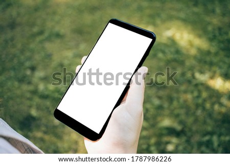 Top view mock up image of woman holding smartphone with blank white desktop screen on grass background
