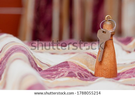 A key on a wooden key chain from a hotel room on a blanket on the bed against the background of a window curtain.