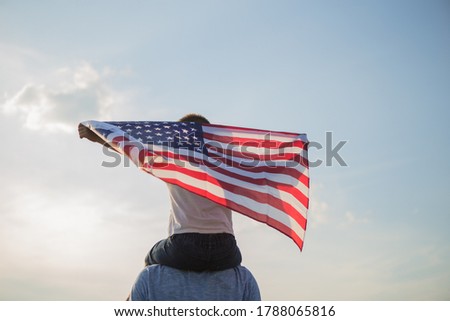 Little boy lets the american flag fly in his hands on the wind at the green field. Patriotic family celebrates usa independence day on 4th of July. Constitution and Patriot Day.