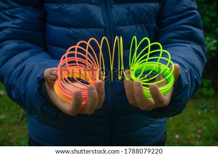 The child's hands hold a spring made of rainbow colored plastic