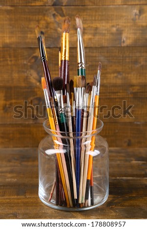 Brushes  in  glass jar on wooden background 