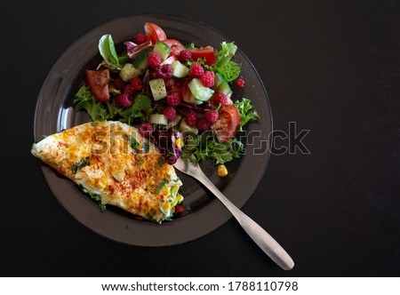 Delicious, healthy salad and omelette on a black background, pictured from above