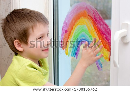 Smiling boy painted a rainbow on the window with paint. Close-up photo, artistically processed. Horizontal.