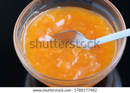 Sweet beautiful apricot jam in a glass rosette that stands on a black mirror surface, macro photography