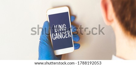 Hand in medical glove holding smartphone on white background. Blank screen with lung cancer text.
