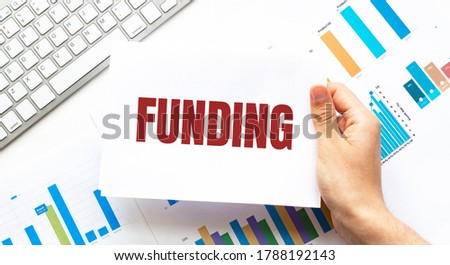 Businessman holding a card with text FUNDING. Keyboard, diagram and white background