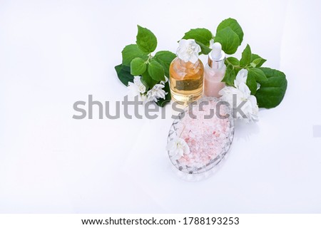 Products for spa treatments in the beauty salon and at home. Jasmine oil essence, cream and pink salt. On a white background with fresh flowers. Free space for text. High quality photo