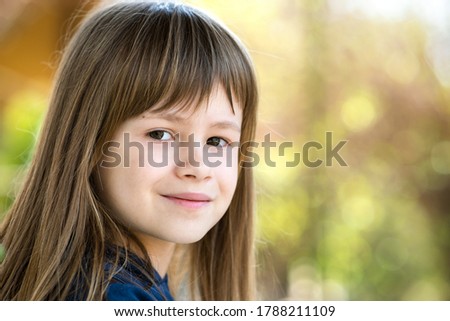 Portrait of pretty child girl with gray eyes and long fair hair smiling outdoors on blurred bright background. Cute female kid on warm summer day outside.