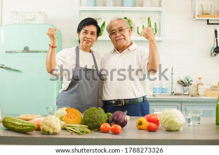 Picture of an elderly Asian couple cooking in the kitchen at home. They have smiles and Flex the arms showing strength. Retirees take care of themselves by choosing healthy food.