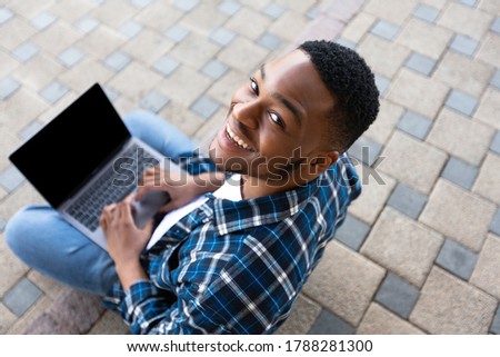 Above view of black man using personal computer sitting on the stairs in city, looking at camera, mock up