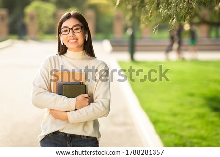 Educational Concept. Portrait of charming young teen girl wearing glasses standing with books and backpack in park