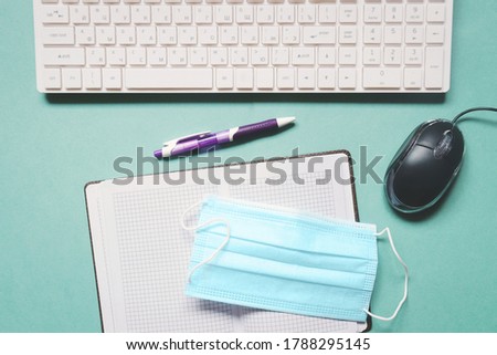 Coronavirus COVID-19 pandemic. Office work, remote job, distance learning. Flat lay photo computer keyboard and mouse, open paper notebook, pen and blue disposable mask