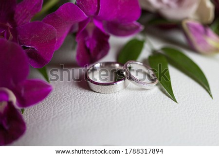 Close up picture of the two new beautiful elegant white gold wedding ring's pair, one is plain, one is with small shiny diamonds, purple and green flowers, white background