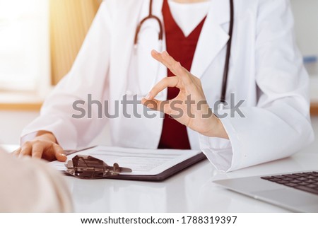 Unknown woman-doctor and patient discussing something while sitting at the table in sunny clinic, close-up