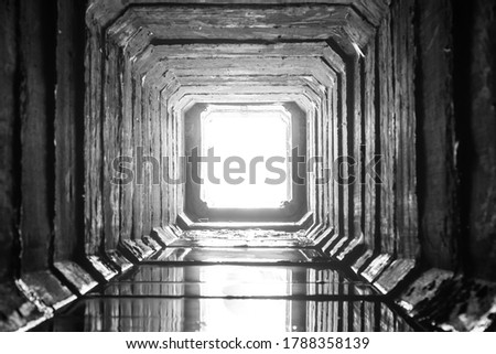 Square concrete drainage tunnel with light in the end, with overexposed white free space.
