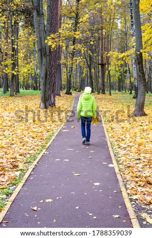Outgoing teenager girl, back view. The concept of the problem of relationship with a child, resentment, quarrel, loneliness, misunderstanding. Walk in the autumn park. Vertical photo