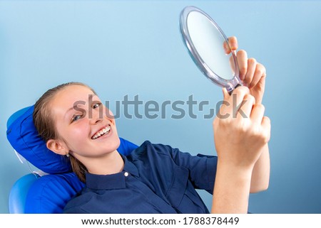 A happy teenage girl looks in the mirror at her teeth in braces and smiles