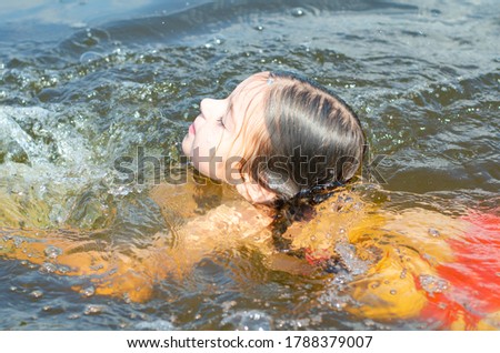 Young six year old girl swimming in a lake on a clear summer day. Caucasian child on vacation outside the city in the village. Holiday concept.