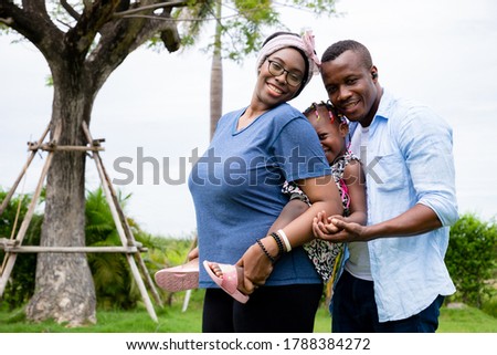 A warm family of black Americans. They have a bright and friendly smile with kiss their daughter. Concepts of relationship building and leisure activities in the garden. Being the best family.