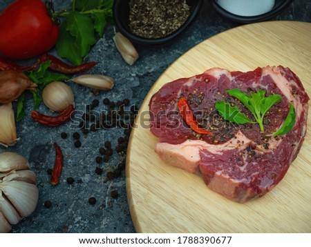 The picture of fresh raw rib eye steak of beef on wooden Board  with salt, pepper and garnish in a simple style.