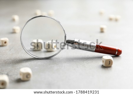 View on cubes with letters A and Q through magnifying glass at light grey stone background, closeup. Find keywords concept