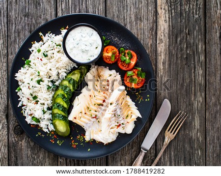 Fish dish - fried cod fillet with basmati rice and vegetables on wooden table
