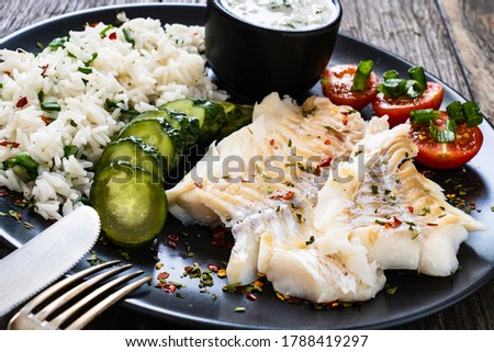 Fish dish - fried cod fillet with basmati rice and vegetables on wooden table