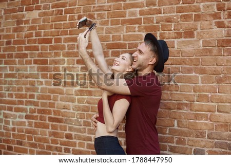 A couple makes a joint photo. The woman and the man are making selfie on the phone.