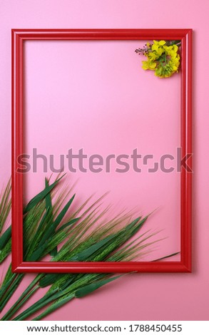 Red wooden picture frame decorated with small yellow flowers, green leaves and wheat heads on pink background.