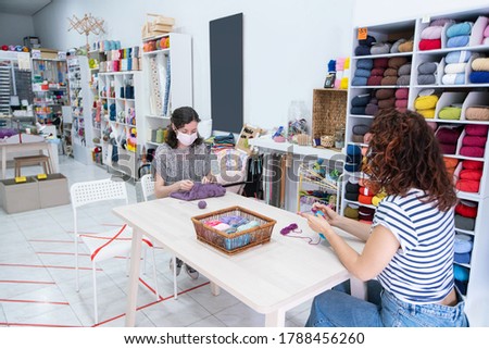 Horizontal view of a knitting workshop on a retail shop. Unrecognizable women wearing face mask practicing knitting with hygienic social distance.