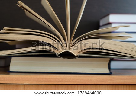 open book in the shape of a fan lies on the table against the background of other books. Home schooling concept, knowledge acquisition.