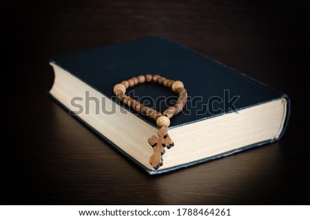 The book lies on a dark wooden table, a wooden rosary with a cross lie on the book. The concept of the Catholic faith.