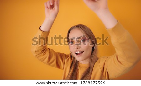 Happy blond girl in party mode dancing, Hands moving in air. Isolated on the orange background. High quality photo