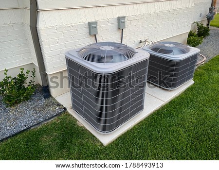 Double AC units outside white brick home with green landscape and gravel Royalty-Free Stock Photo #1788493913