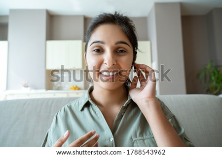 Smiling indian woman professional online teacher, telesales agent, remote tutor or call center operator wearing headset look at webcam conference video call center at home office. Headshot portrait. Royalty-Free Stock Photo #1788543962