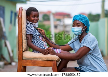 African health worker wearing a surgical face mask and child wearing homemade mask for protection,auscultating child chest,both looking at camera-concept on child health in covid-19 pandemic Royalty-Free Stock Photo #1788550157