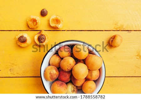 ripe juicy homemade apricots with cracks and flaws in the plate and scattered on a bright yellow wooden surface. Harvest 2020