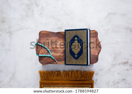 Islamic concept - The Holy Al Quran with written Arabic calligraphy meaning of Al Quran and rosary beads or tasbih and prayer rug, on wooden stand, with copy space. Royalty-Free Stock Photo #1788594827