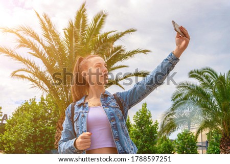 Making picture. Pretty female taking fun self portrait photo. Happy young girl with phone smile, typing texting and taking selfie in summer sunshine urban city. Vanity, social network concept.