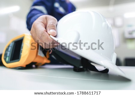 The engineer picks up the white helmet placed on the office desk with a blurred background. The concept of work safety in the construction area. Royalty-Free Stock Photo #1788611717