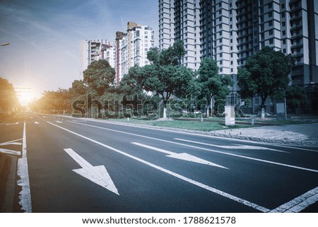 Clear sky, asphalt road with traffic guide lines beside high-rise buildings in the city