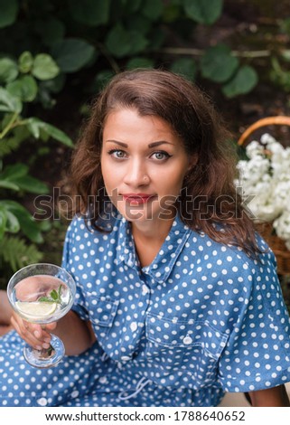 Summer picnic. A girl in a summer blue dress and a straw hat sits on a picnic in nature and drinks mojito. Picnic with baguettes, grapes, cherries and cocktail.