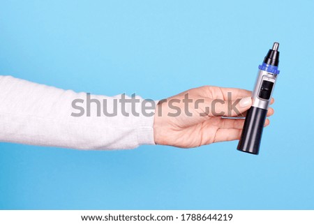 Hand with nose trimmer, hair electric cutter. Isolated on blue background.