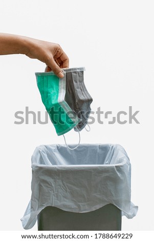 Hand put the disposable surgical mask in the gray colour trash can. The right way to throwing used face mask in the bin isolated on white background  Covovirus or Covid-19 concept.