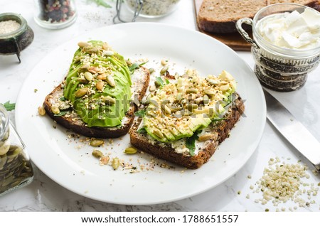 Healthy avocado toasts for breakfast or lunch with rye bread, cream cheese, arugula, sliced avocado, pumpkin, hemp and sesame seeds, salt and pepper. Vegetarian sandwiches. Clean eating. Royalty-Free Stock Photo #1788651557
